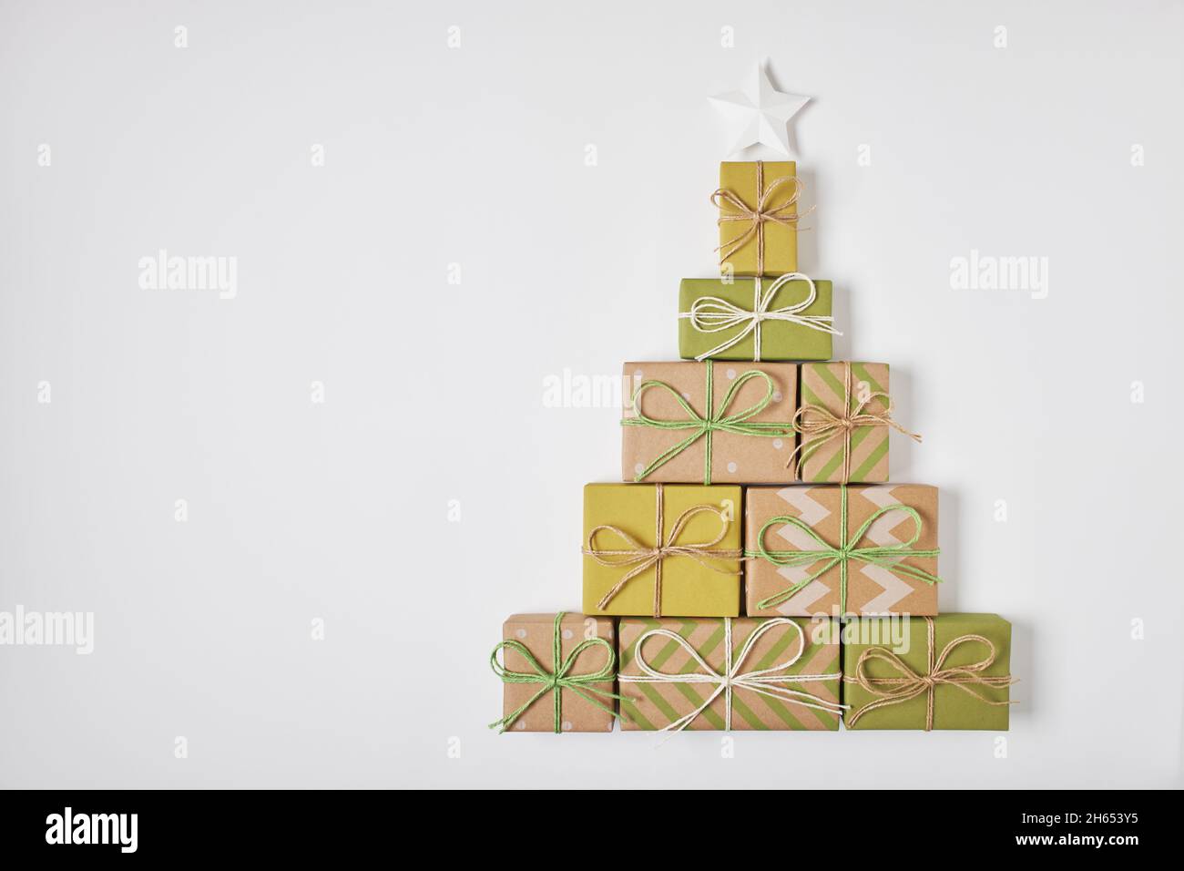 Albero di Natale fatto di regali e stella decorativa su sfondo bianco. Vista dall'alto, disposizione piatta, spazio di copia. Foto Stock