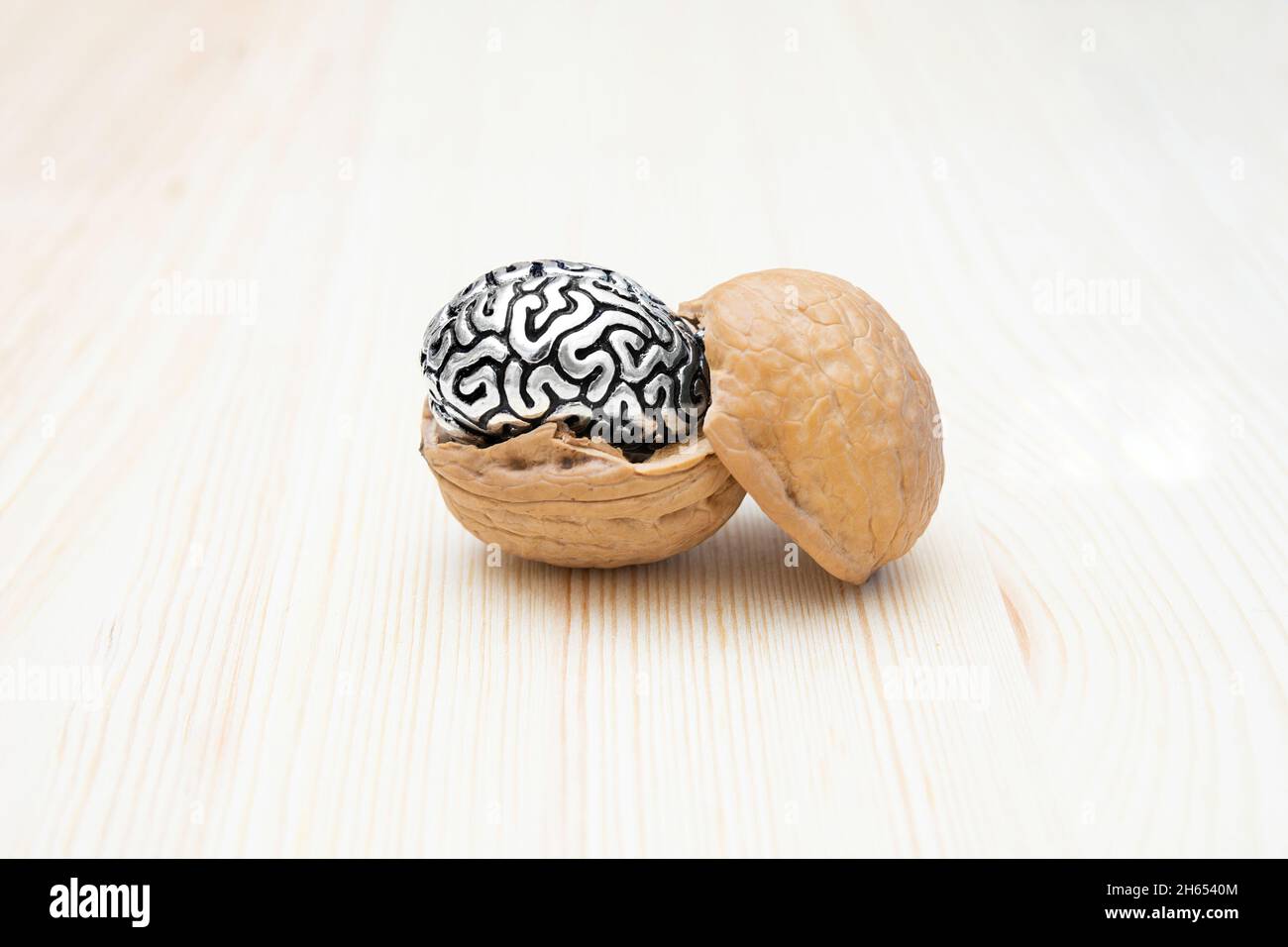 Guscio di noce con una copia in acciaio miniaturizzato di un cervello umano all'interno su un tavolo di legno. Concetto naturale di supercibo e salute mentale. Foto Stock