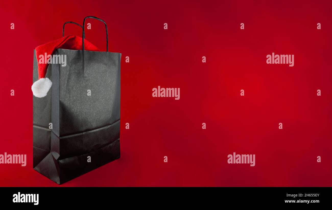 Su sfondo rosso è una borsa di carta nera con un cappello Babbo Natale all' interno. C'è molto spazio per le copie Foto stock - Alamy