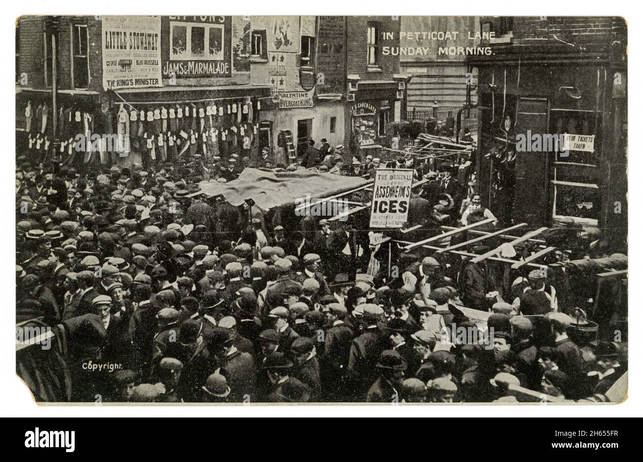 Cartolina originale di auguri dell'epoca edoardiana di tutti gli uomini di folla, classe di lavoro, con cappelli piatti, in Petticoat Lane, abbigliamento in vendita, Domenica mattina, Londra, Regno Unito circa 1907 Foto Stock