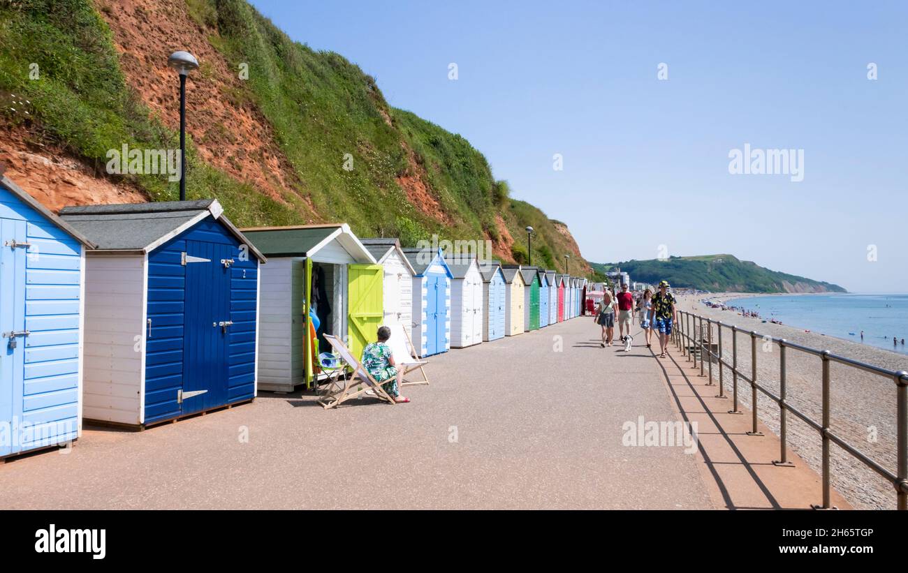 Seaton Devon persone prendere il sole vicino alle capanne sulla spiaggia lungo la passeggiata a Seaton Devon Inghilterra UK GB Europa Foto Stock
