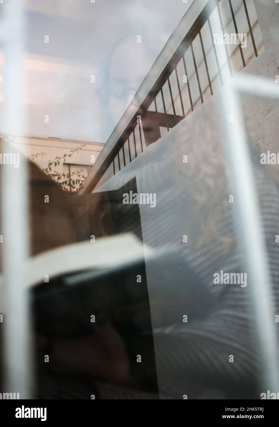 Bel ritratto caldo attraverso la finestra con gocce d'acqua di giovane adulto lettura in una giornata piovosa Foto Stock