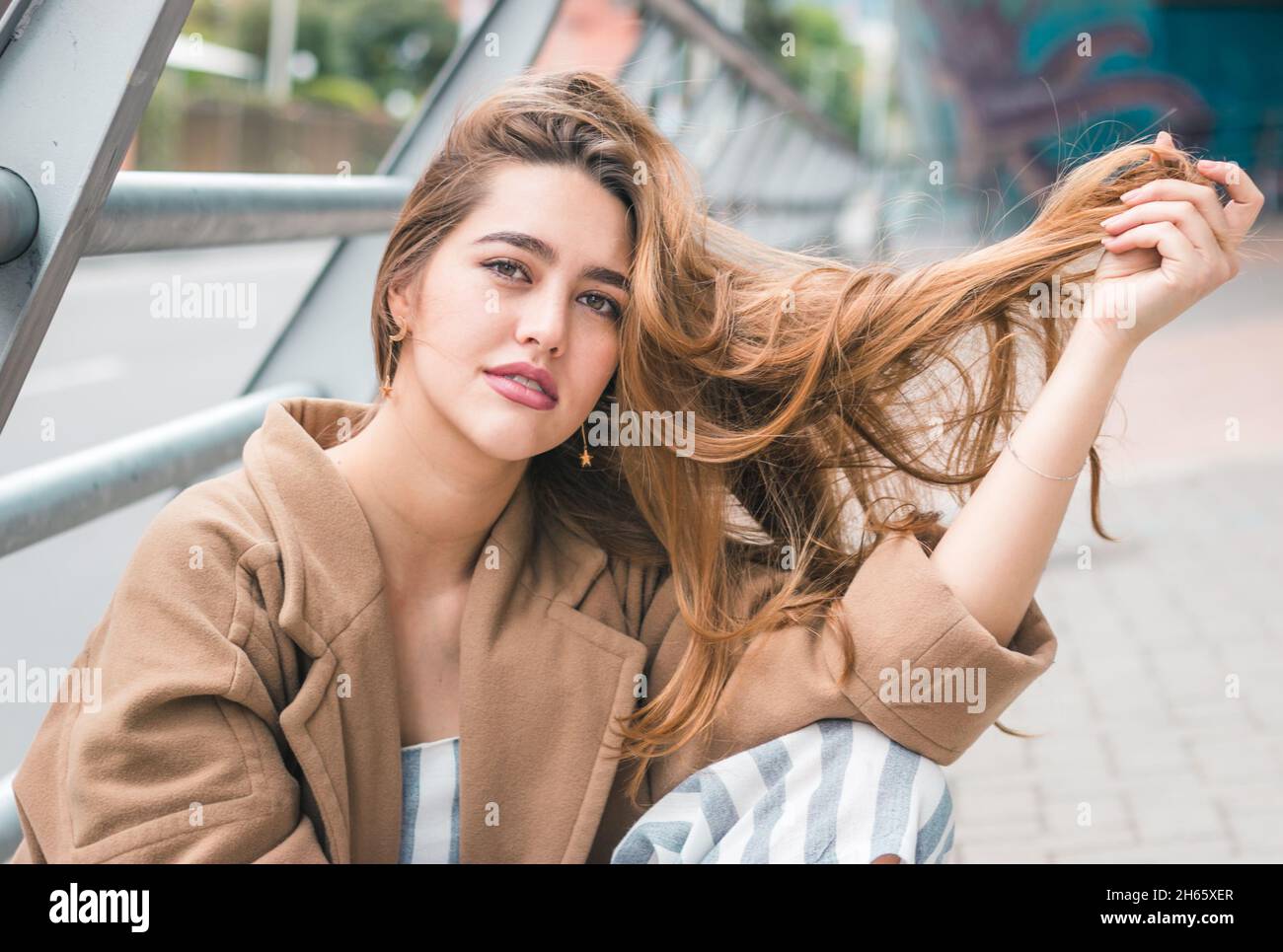 Bella donna colombiana si siede e si pone in ambiente urbano - capelli d'oro rosso e linee guida Foto Stock
