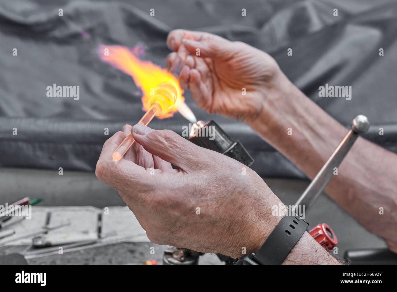 Processo di lavorazione artistica del vetro mediante fiamma del bruciatore. Mani di soffiatore di vetro maturo Foto Stock