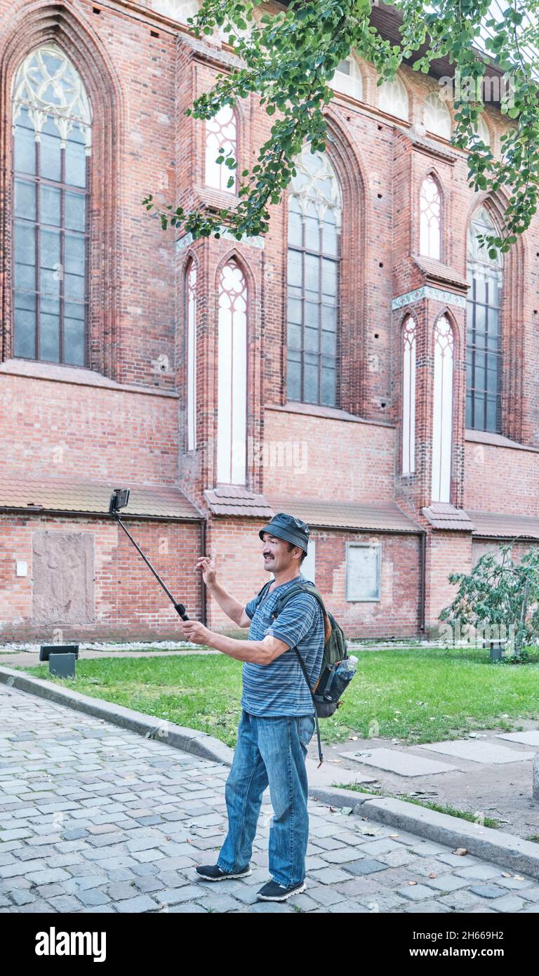 Video di tiro del blogger asiatico maturo per il suo blog sul social network vicino al muro della Cattedrale, Kaliningrad, Russia Foto Stock