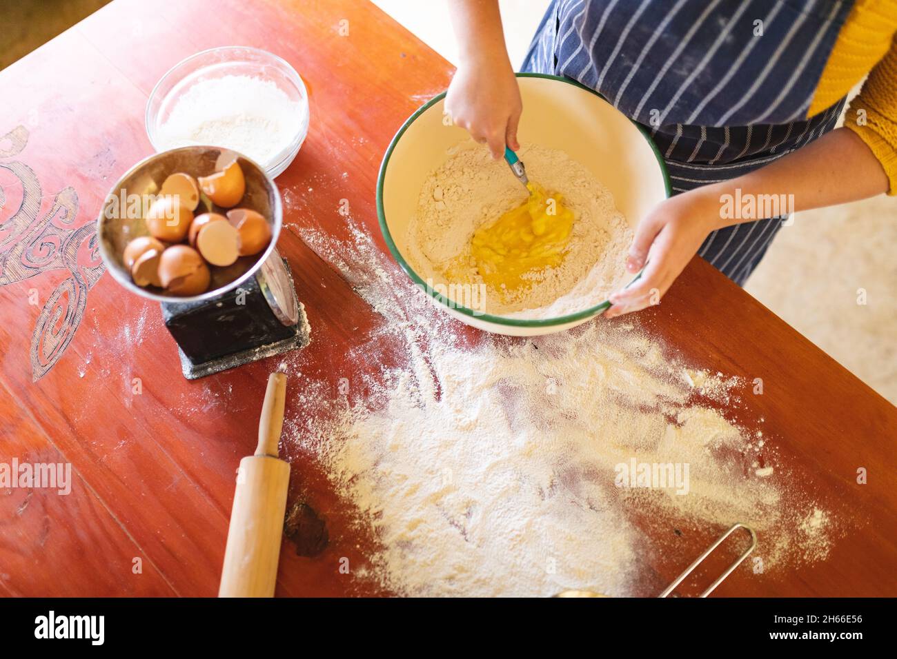 Metà della donna mescolando tuorlo d'uovo e farina in una ciotola con cucchiaio al tavolo Foto Stock