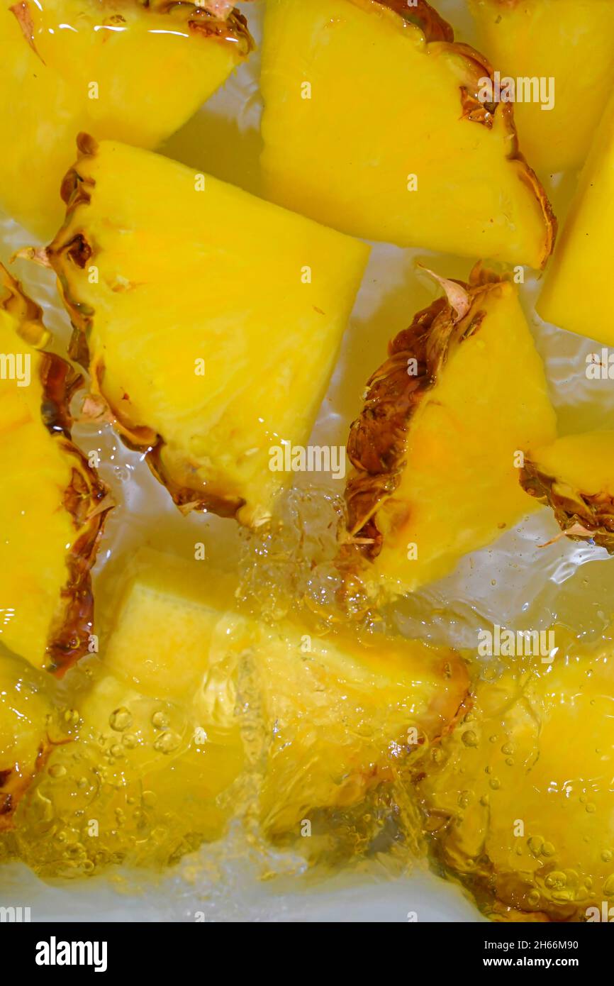Primo piano di ananas in liquido con bolle. Fette di ananas matura in acqua. Primo piano fette fresche di ananas giallo su sfondo bianco. Verticale Foto Stock