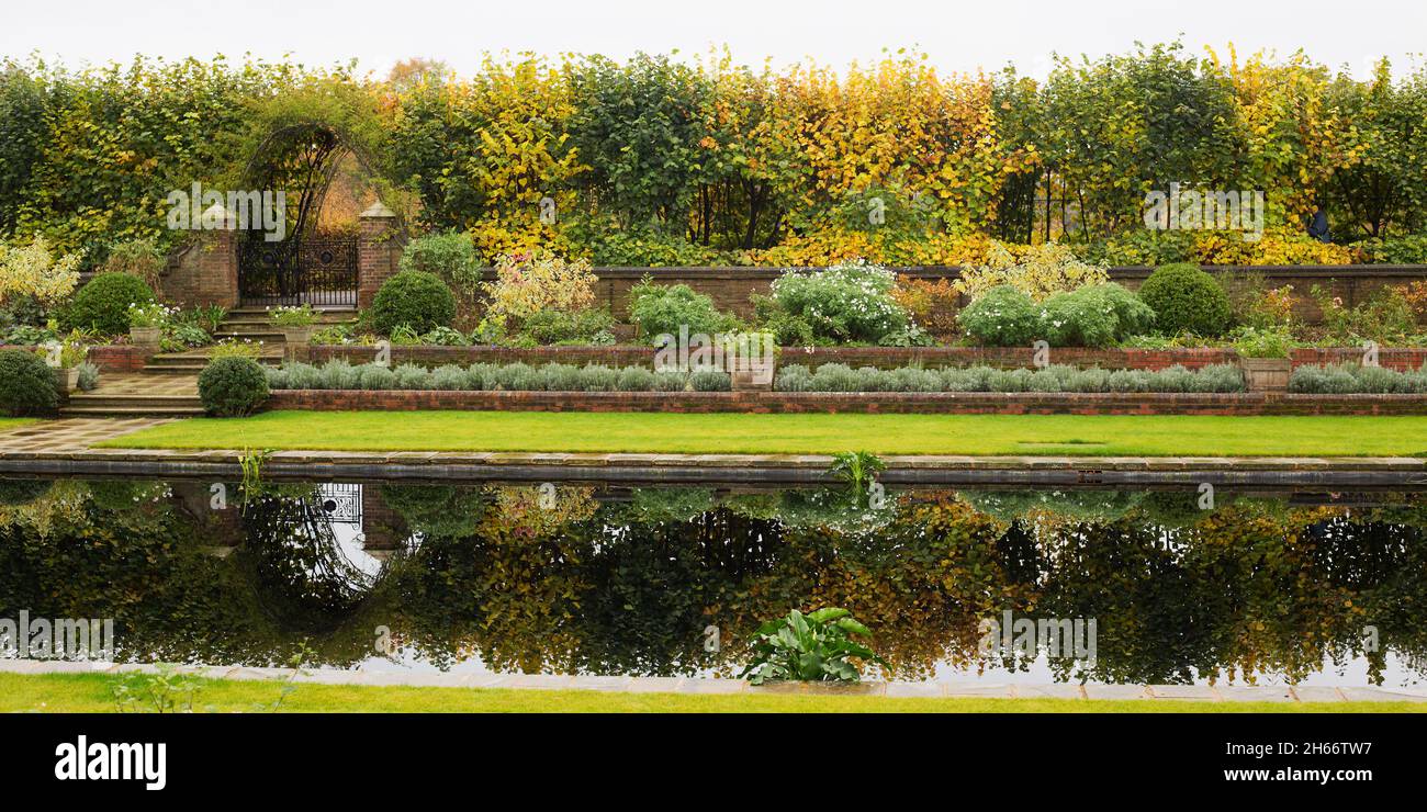 Panorama di una giornata autunnale con aiuole e giardino murato, contro un laghetto ancora riflettente. Foto Stock