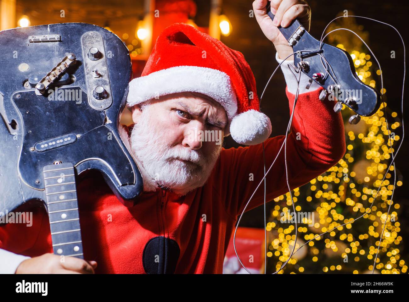 Uomo barbuto in costume di Santa con chitarra elettrica rotta. Strumento musicale. Chitarrista rock. Anno nuovo. Natale. Foto Stock