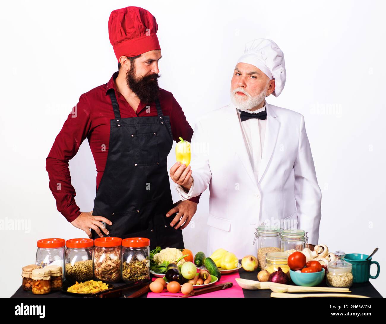 Due cuochi in uniforme si trova vicino al tavolo con verdure. Chef con assistente in cucina pronto per cucinare. Cucina professionale. Cibo sano Foto Stock