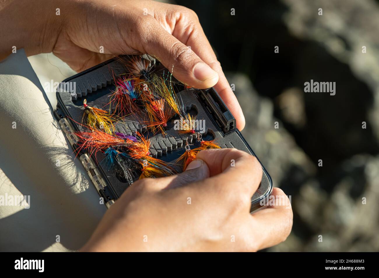 Un primo piano di una femmina asiatica che seleziona la pesca del mosca del salmone vola da una scatola Foto Stock