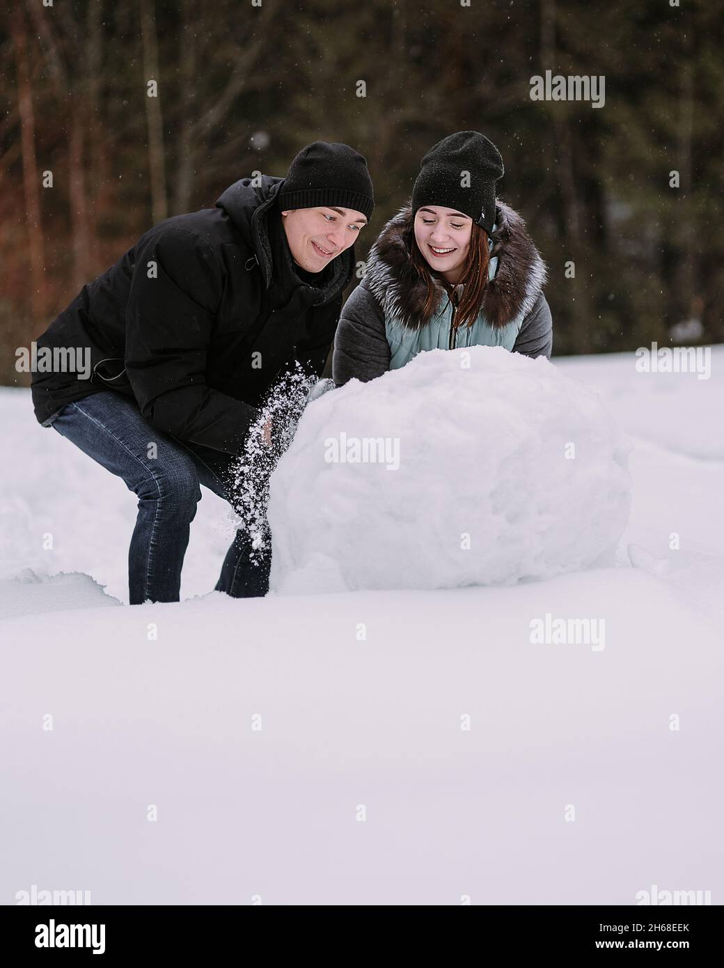 Coppia di adolescenti che costruiscono pupazzo di neve insieme nella foresta invernale Foto Stock