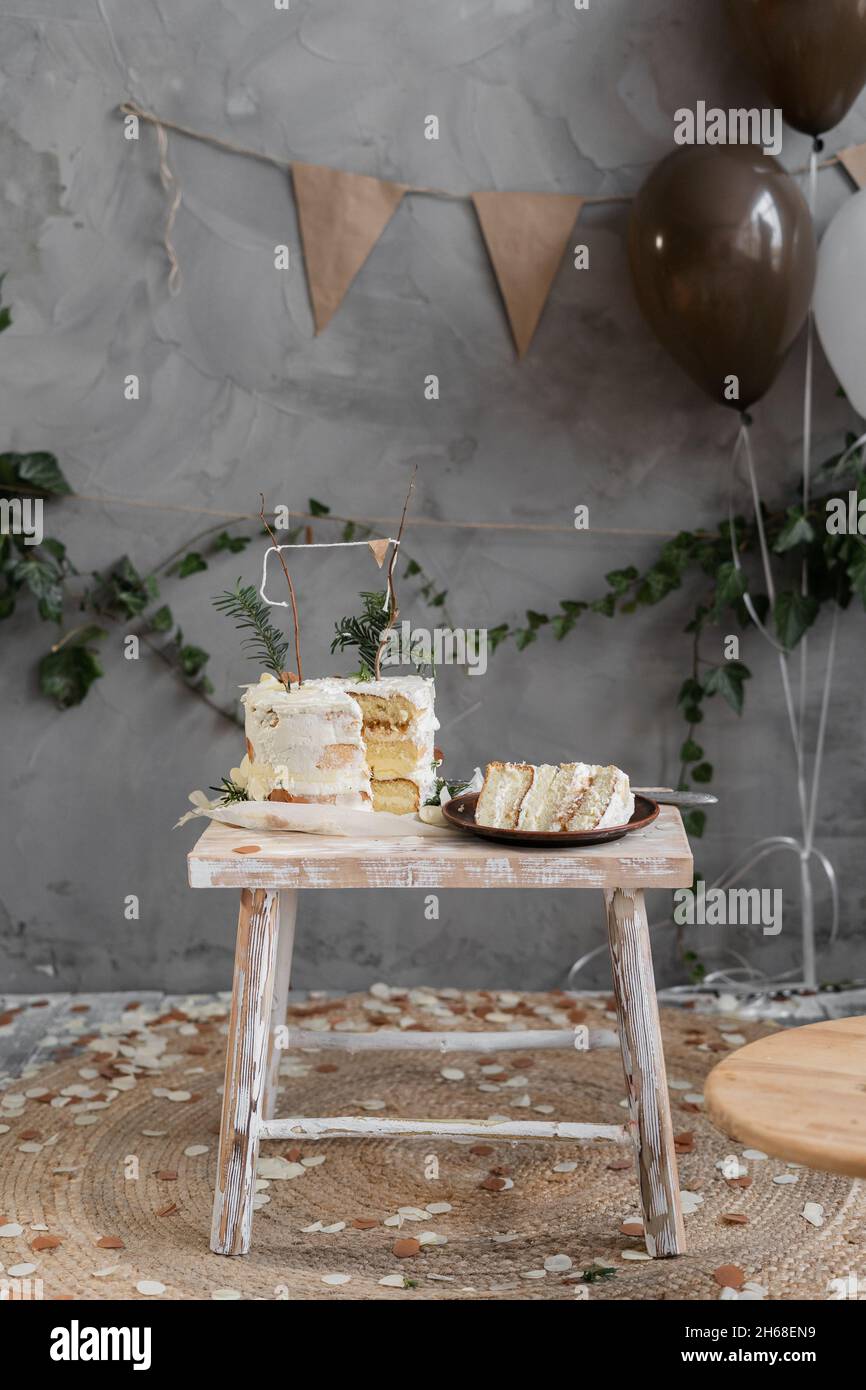 Decorata con torta alla crema per il primo compleanno, posta su un piccolo  tavolo di legno, un pezzo di torta tagliato su un piatto, una stanza con decorazioni  fatte a mano Foto