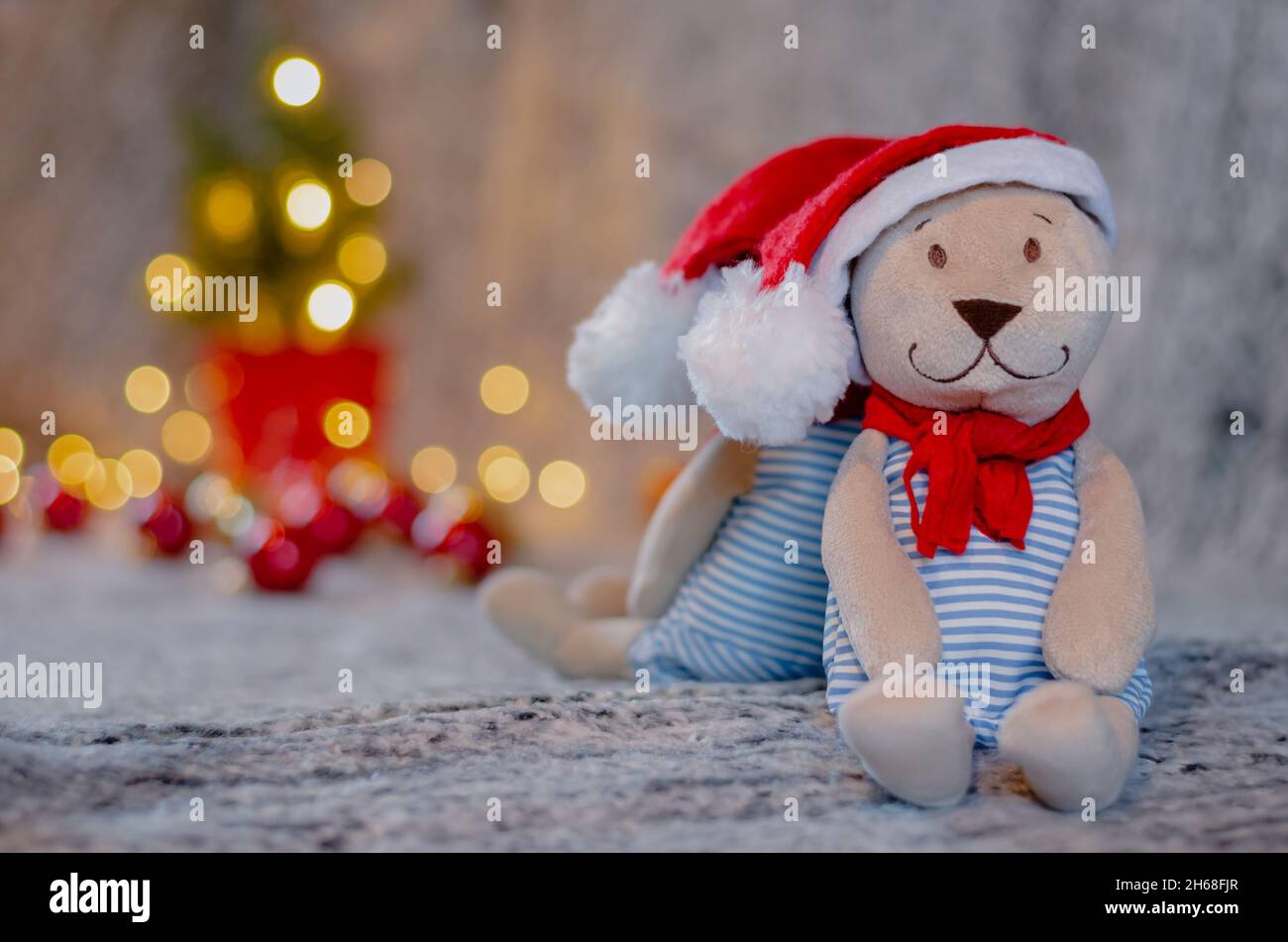Bambola di orsacchiotto con cappello e scarpetta di santa con bokeh sfondo chiaro dell'albero di Natale. Foto Stock