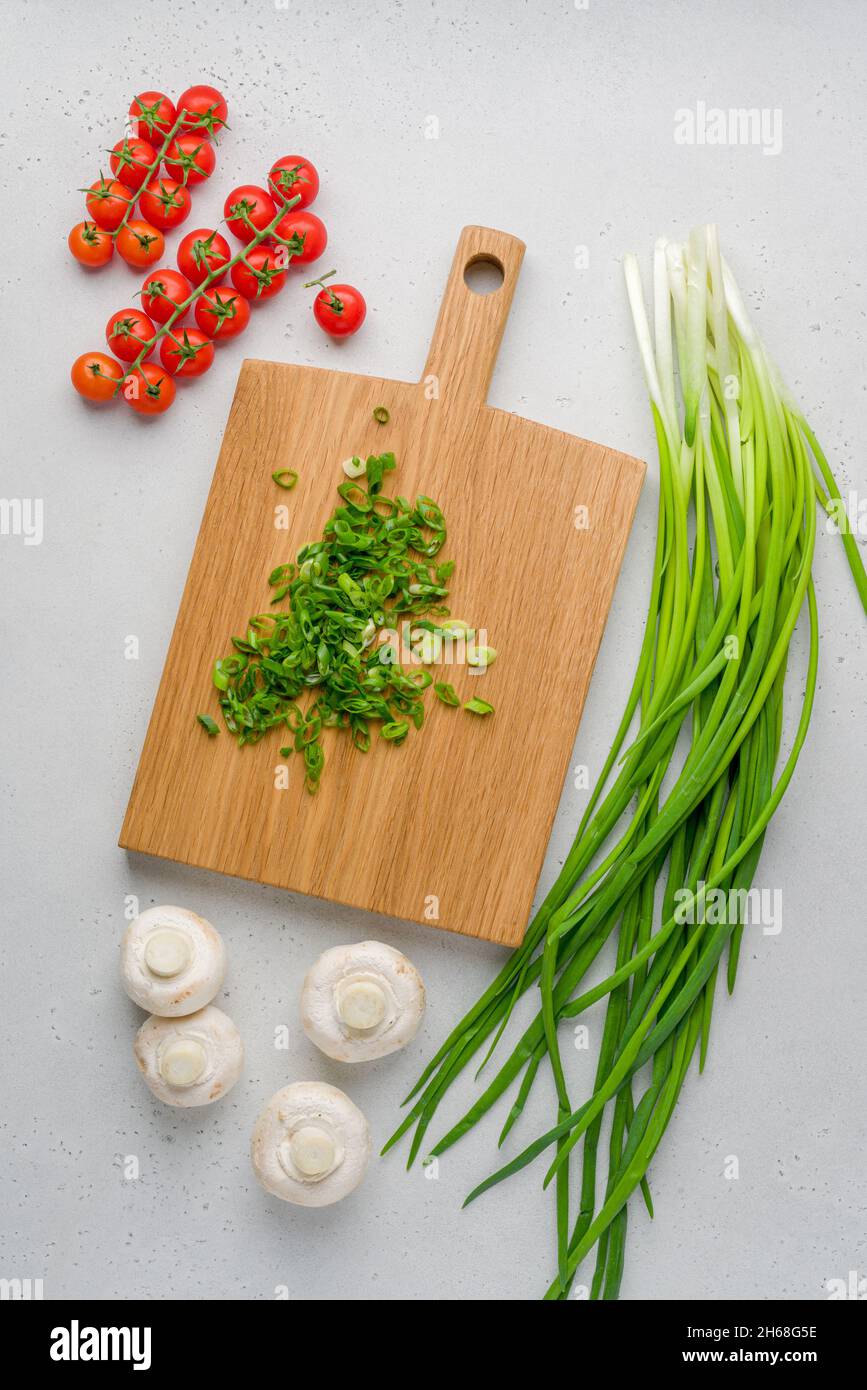 Ingredienti freschi preparati per la cottura. Pomodori ciliegini, scalpello verde, champignon su tavola di legno. Prodotti naturali e vegetali. Piano cucina Foto Stock