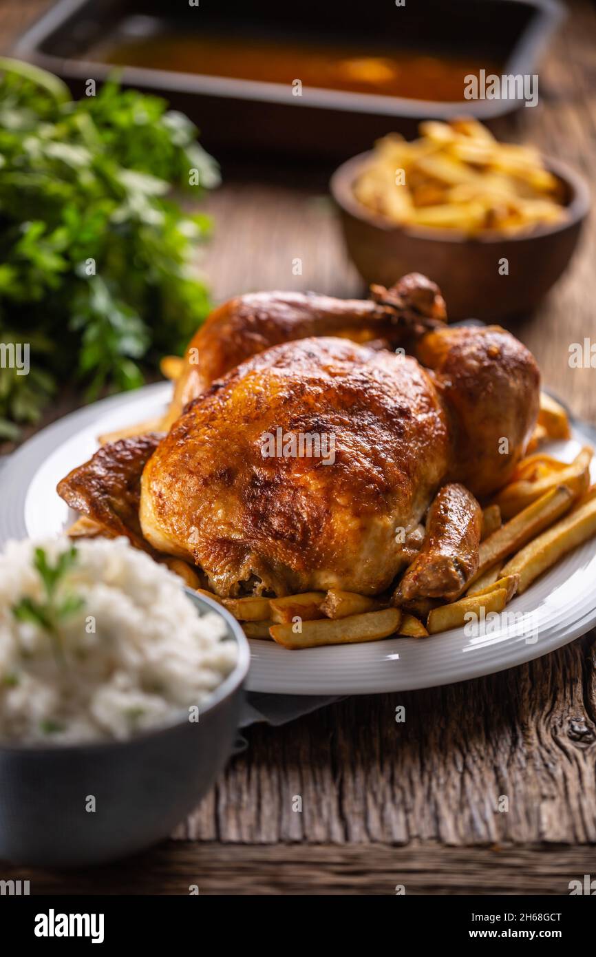 Arrosto di pollo intero su un tagliere di legno con contorni di riso e patatine fritte. Foto Stock