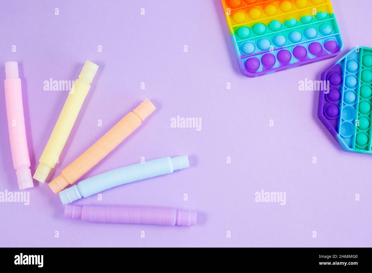 Tubo corrugato in plastica brillante multicolore e pop-it su sfondo viola. Giocattolo in plastica figet sensoriale antistress 2021. Foto Stock