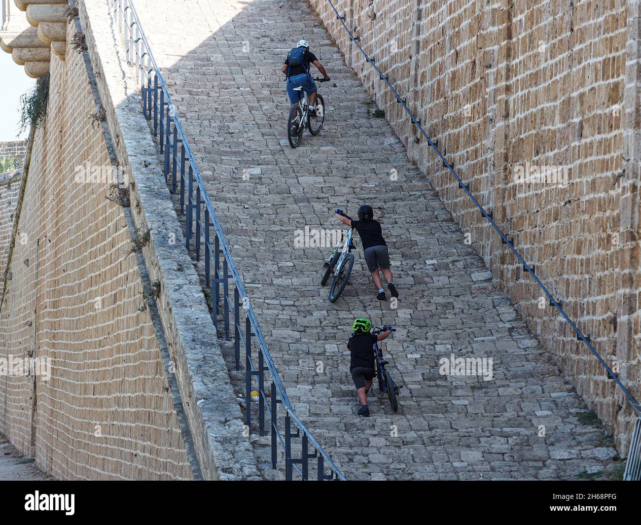 Papà e bambini salgono il muro di pietra su biciclette. Foto Stock