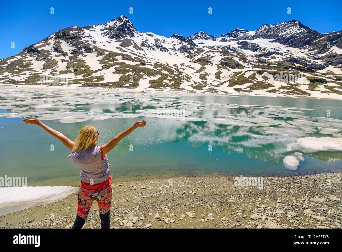 Donna sportiva da trekking a braccia aperte riflettendo il lago bianco in Svizzera. Ghiaccioli sul lago bianco ghiacciato nel Canton Grigioni al passo Bernina Foto Stock