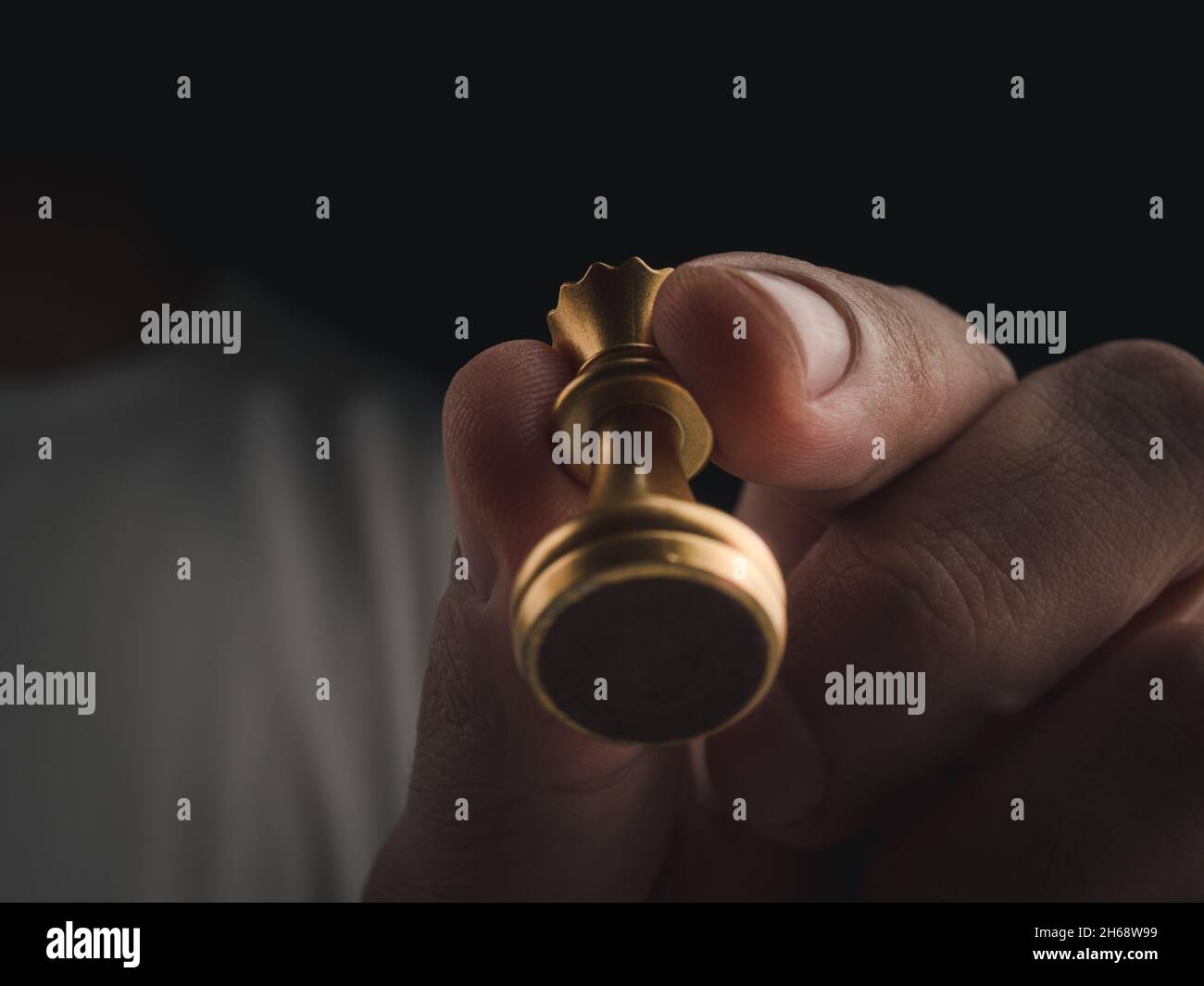 Primo piano in oro regina scacchi pezzo in mano umana in aria su sfondo scuro, sotto vista. La figura di scacchi della regina di movimento della mano sulla concorrenza di gioco di scacchi. Il Foto Stock