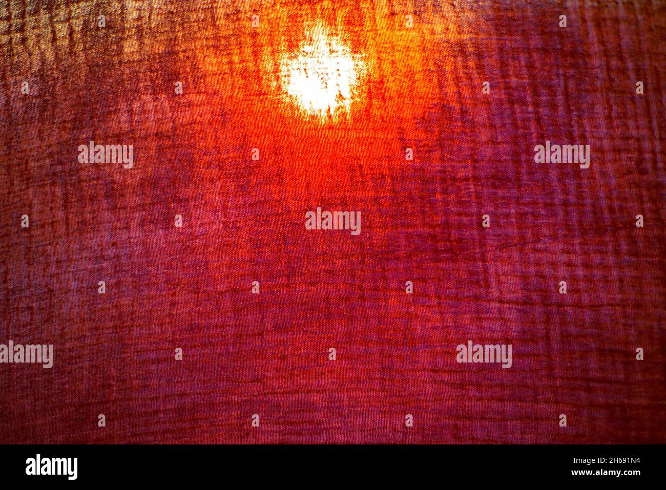 Il sole arancione splende attraverso un tessuto scuro traslucido sfondi Textures Foto Stock