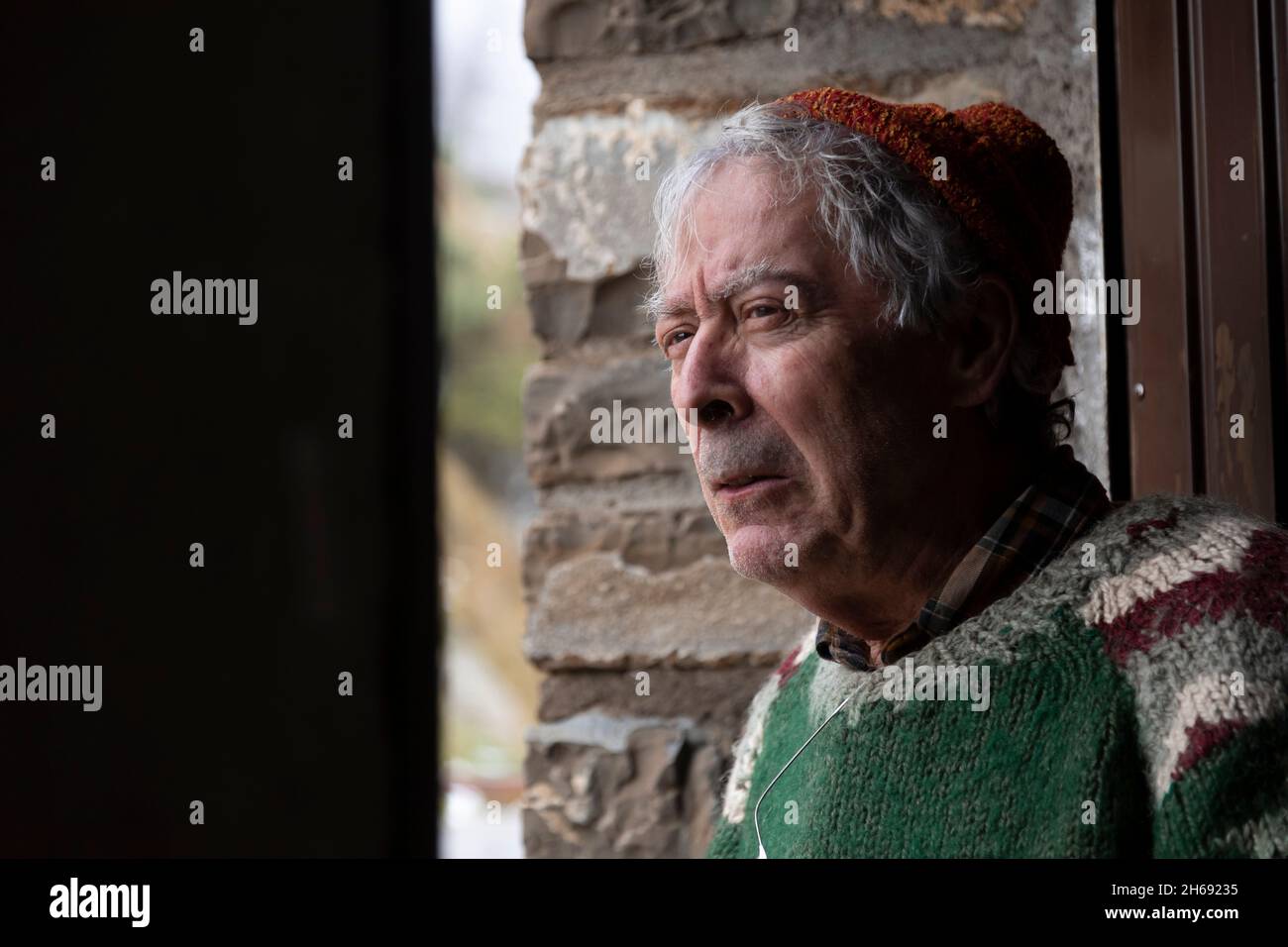 Un alpinista, uomo adulto anziano, nei suoi anni '70, con maglione di lana fatto a mano, osserva l'esterno dalla porta di un rifugio di montagna, Pirenei, Spagna Foto Stock