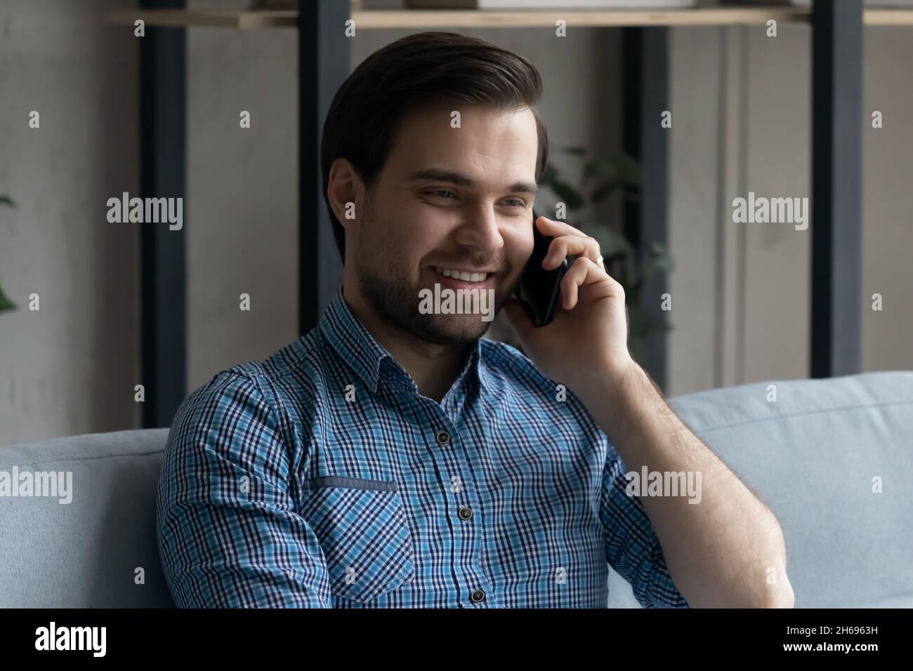 Sorridente bel giovane uomo coinvolto in una piacevole conversazione con lo smartphone. Foto Stock