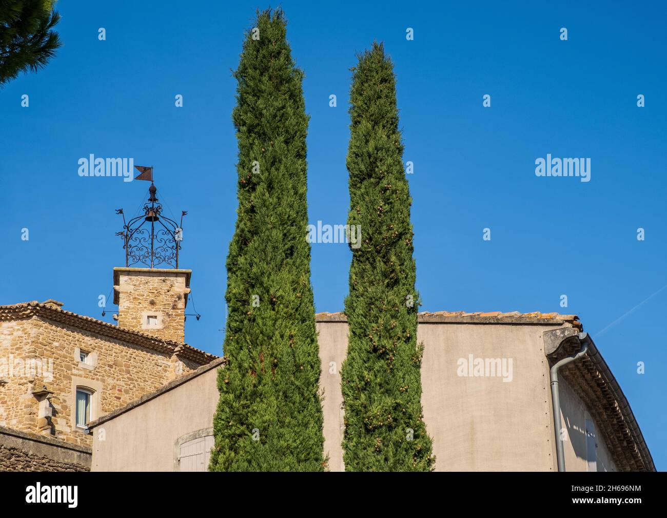 Torre dell'orologio sopra il villaggio di Grillon, Vaucluse, Francia - due cipressi in primo piano Foto Stock