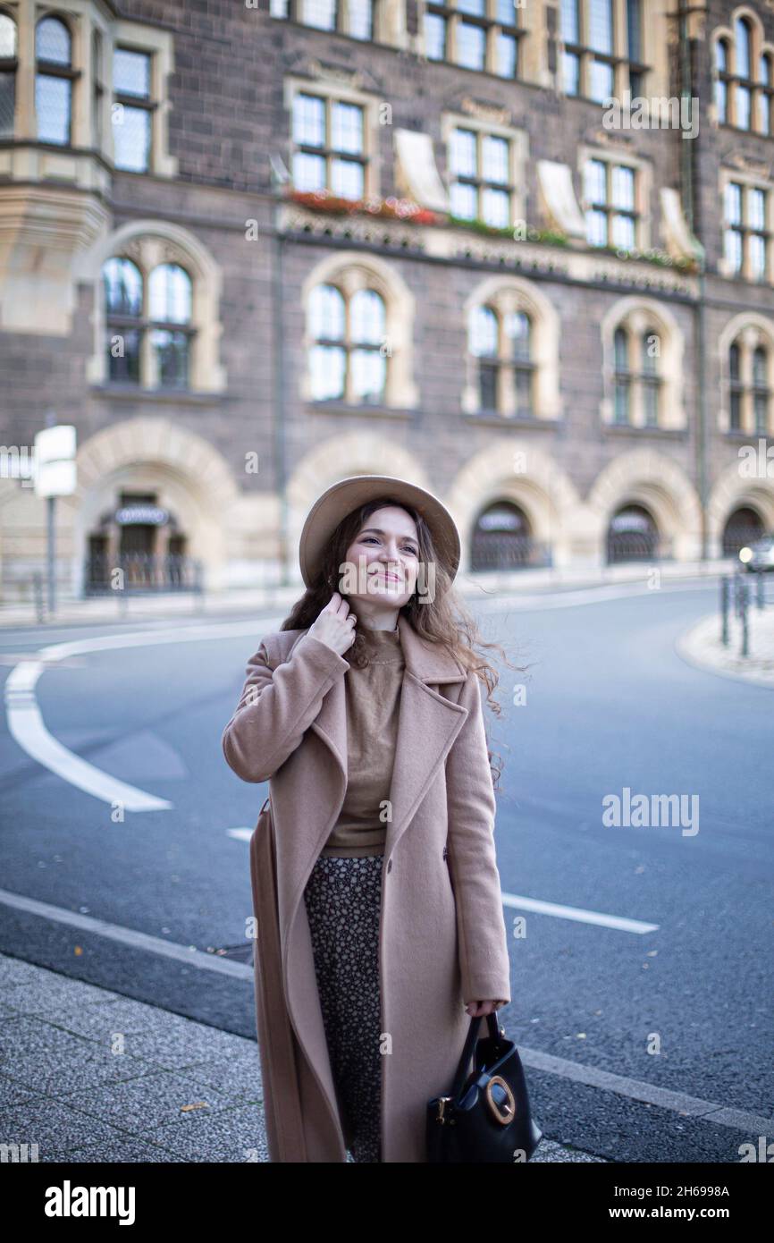 Bella donna con capelli ricci nella città vecchia vestita con cappotto d'autunno e un cappello Foto Stock