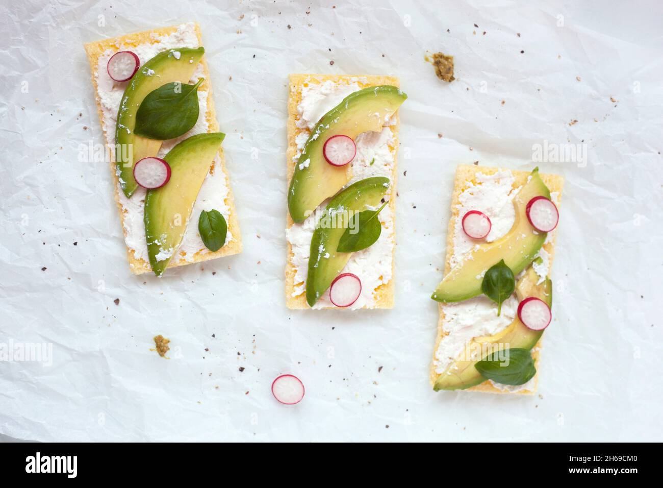 tostatura croccante senza glutine con formaggio morbido, avocado, rafano e basilico su sfondo bianco, vista dall'alto Foto Stock