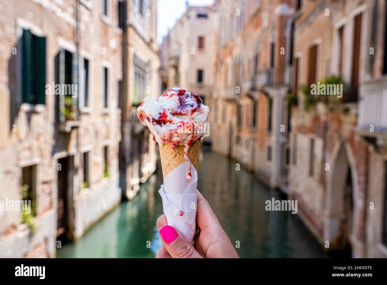 Primo piano della mano tenendo il cono gelato alla fragola davanti al canale Foto Stock