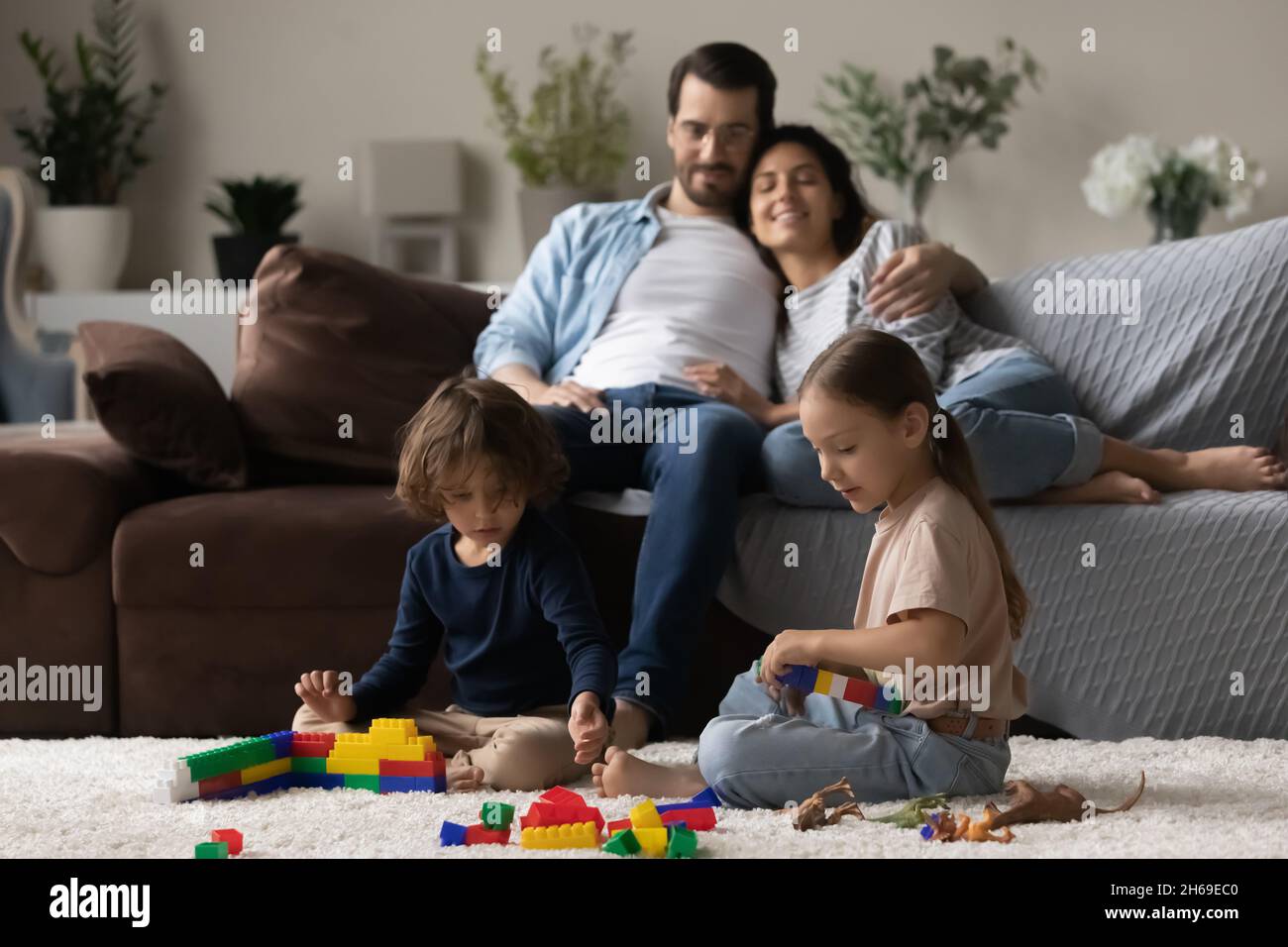 Due bambini insieme mentre il genitore si rilassa sul comodo divano Foto Stock