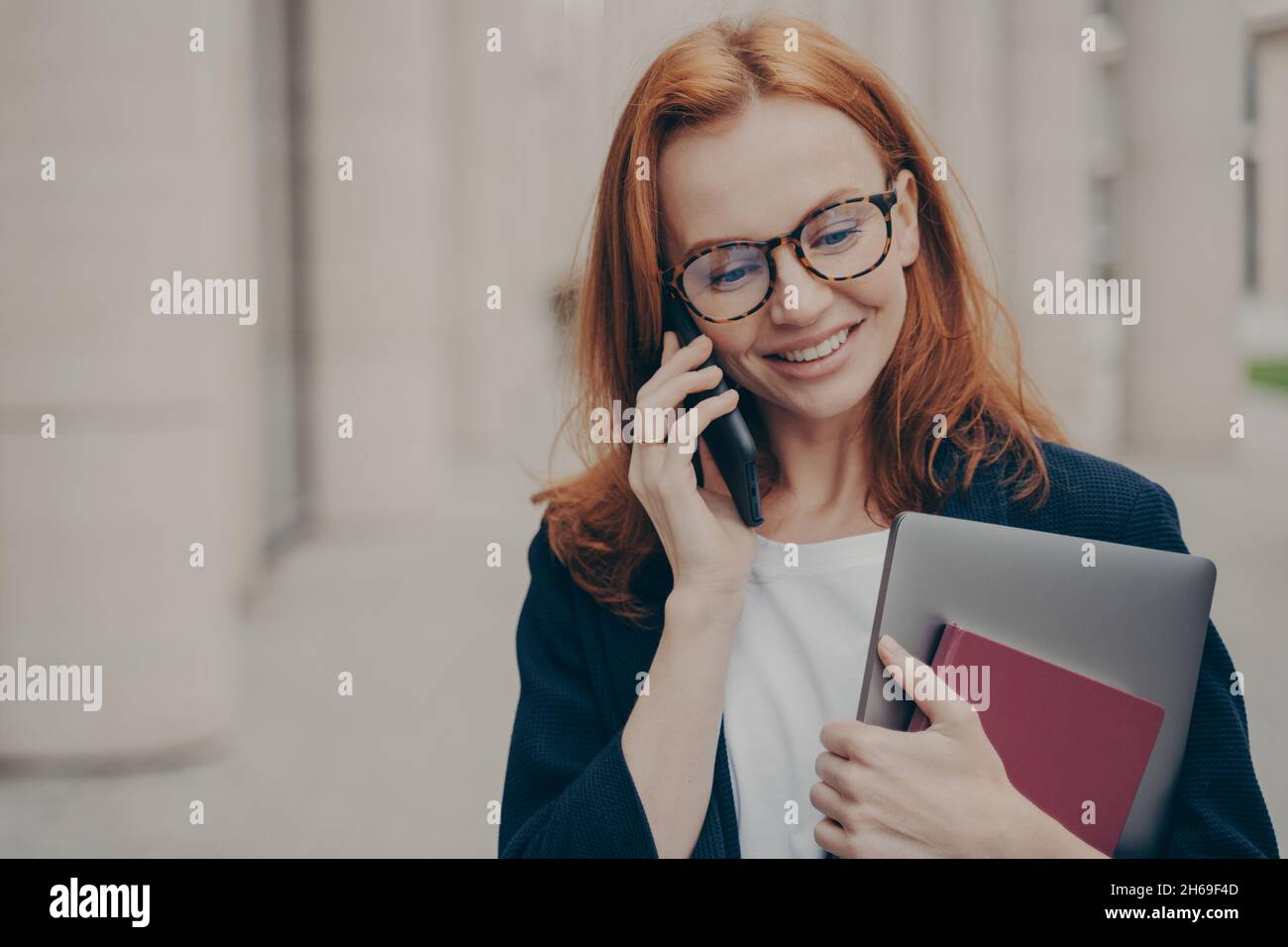 Giovane donna caucasica da 30 anni in piedi all'aperto e parlare con il cliente su smartphone Foto Stock