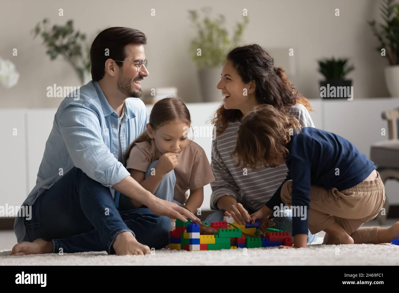 Genitori felici e due bambini che giocano con i giocattoli sul pavimento Foto Stock