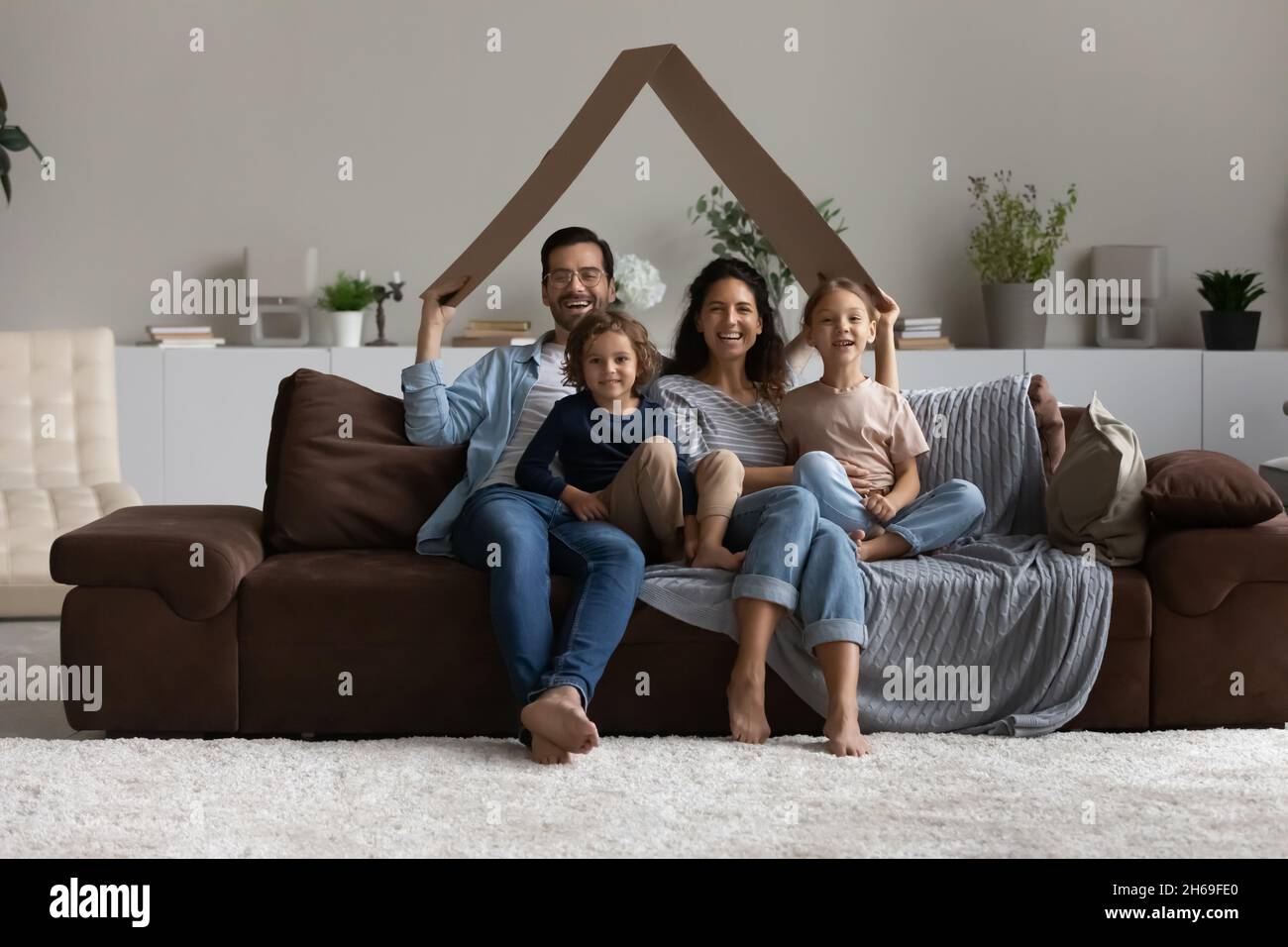 Ritratto di famiglia felice seduto sul divano sotto il tetto di cartone Foto Stock