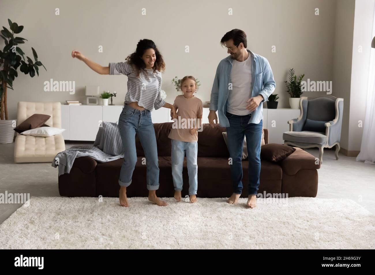 Genitori felici con la figlia che saltano insieme nel soggiorno moderno Foto Stock