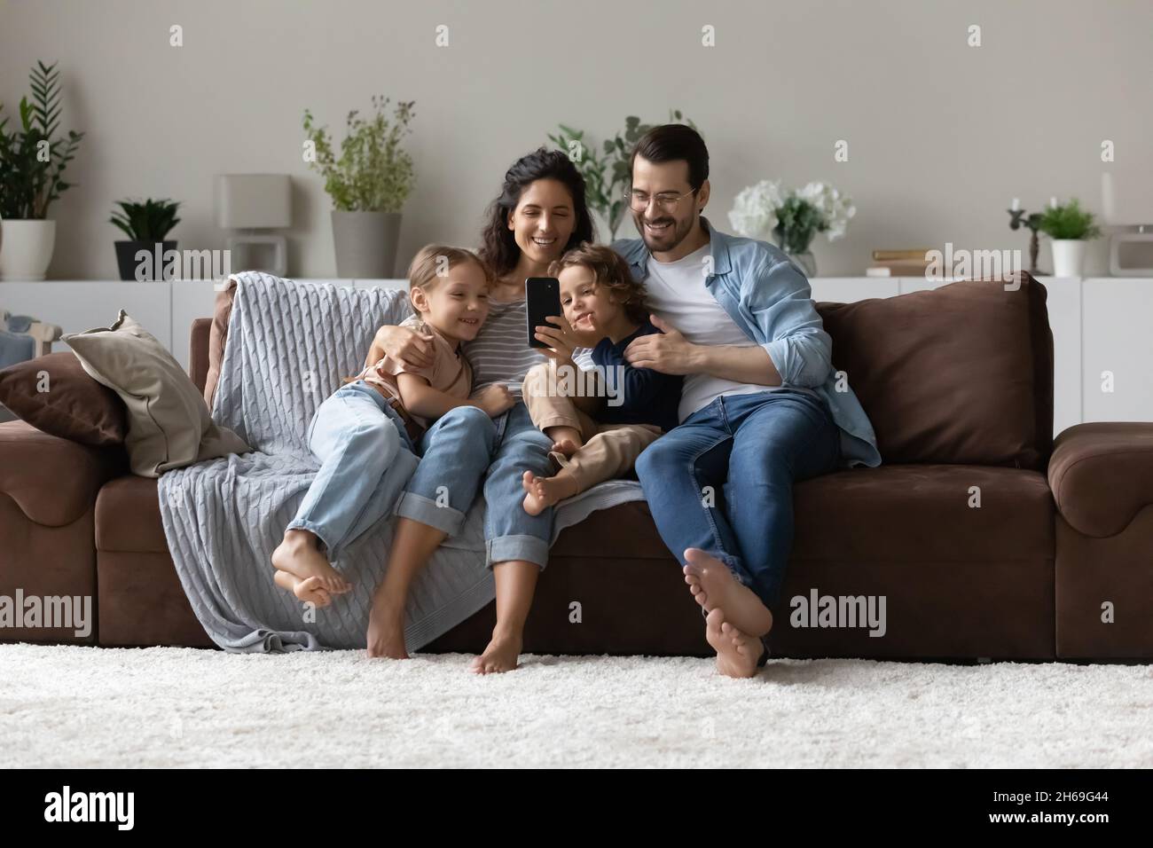Felici i genitori con due bambini che usano lo smartphone a casa insieme Foto Stock