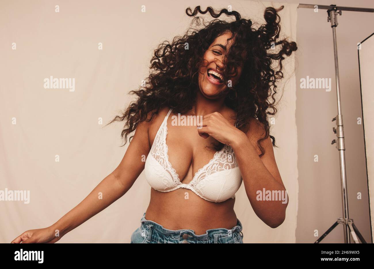 Divertimento in studio. Felice giovane donna ridendo e frustando i capelli mentre si trova in piedi su uno sfondo studio. Corpo positivo giovane donna sentirsi a proprio agio Foto Stock