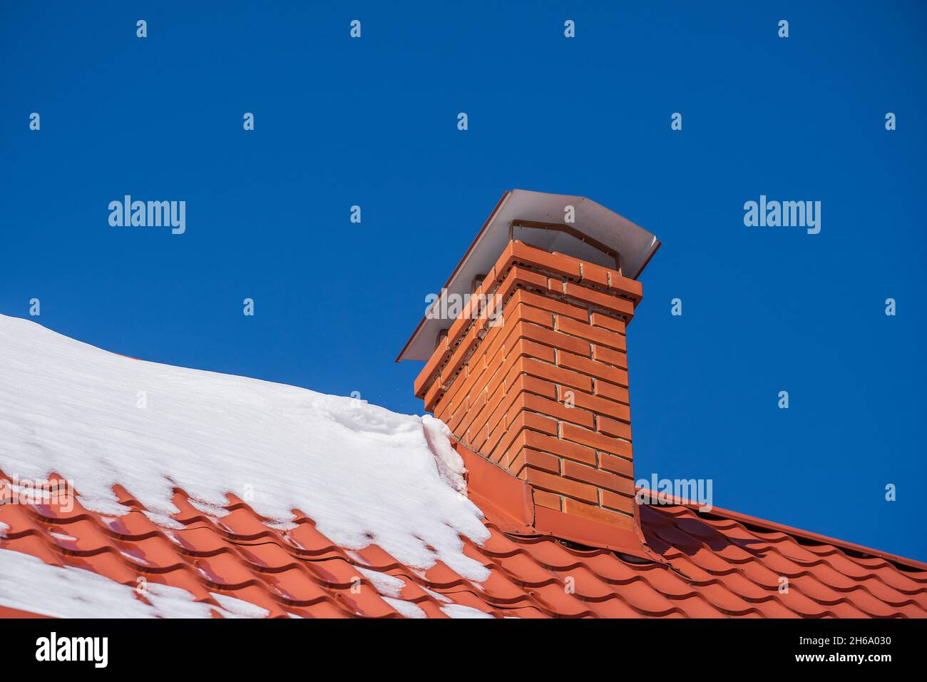 Tetto rosso di una casa indipendente e camino e neve contro il cielo blu in inverno, da vicino Foto Stock