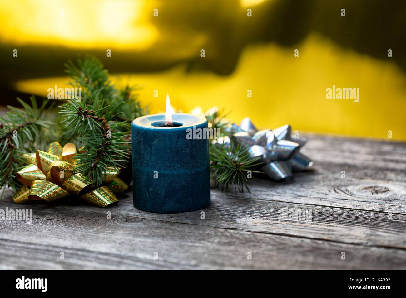 Primo piano di una candela blu che brucia con uno sfondo dorato brillante più rami di abete e fiocchi regalo lucidi per un buon Natale o felice anno nuovo Foto Stock