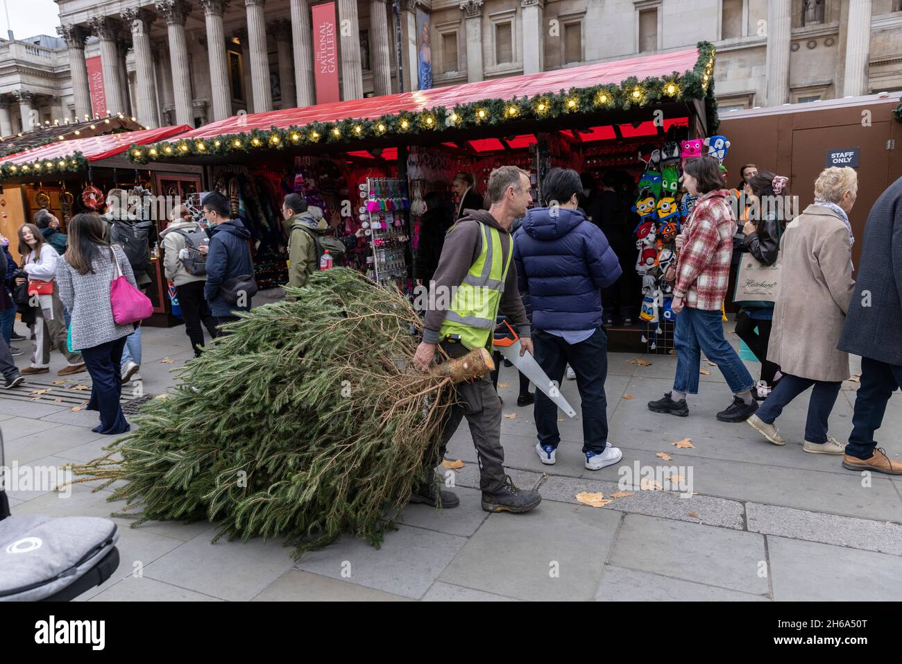 Un lavoratore porta un albero di Natale al mercato di Natale, Trafalgar Square, all'inizio della stagione festiva 2021 Natale nella capitale, Londra, Inghilterra. Foto Stock