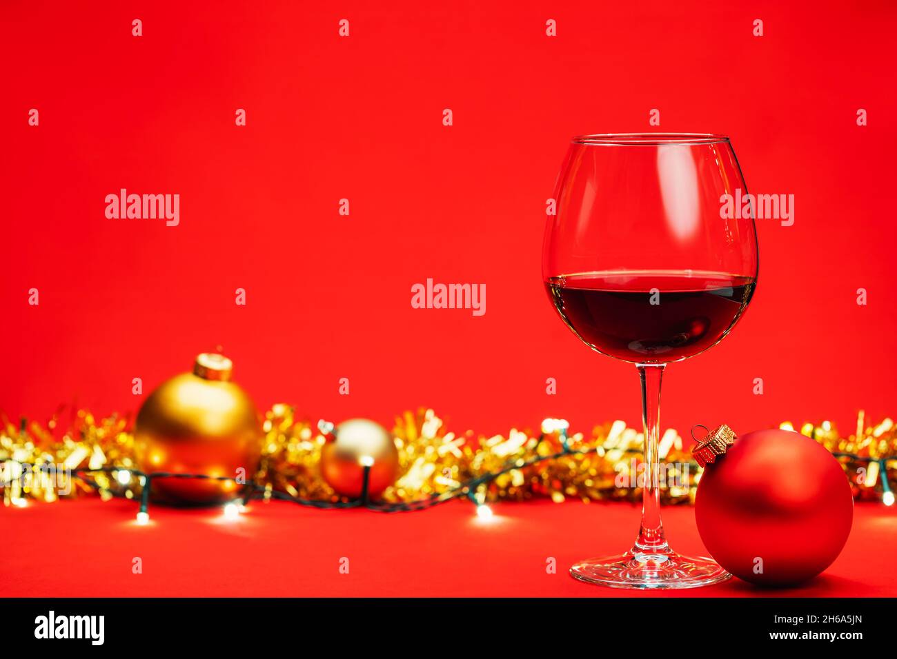 Bicchiere di vino rosso con tinsel baubles di natale e luci su sfondo rosso - concetto di bevanda di natale Foto Stock