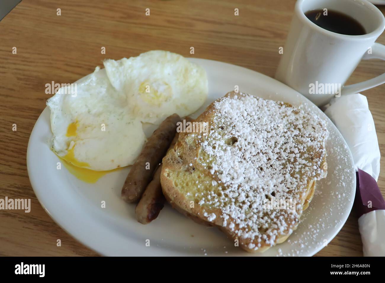 Toast alla francese dall'aspetto delizioso con uova di zucchero in polvere e salsicce sul lato con caffè Foto Stock