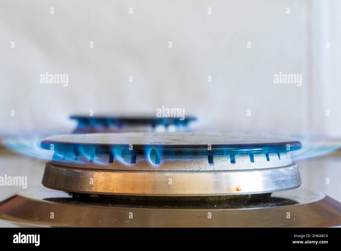Annello a gas acceso sul piano cottura a gas. Anello circolare grigio sormontato da parte superiore in ghisa nera, fiamme blu dalle bocchette di ventilazione sul lato dell'anello. Foto Stock