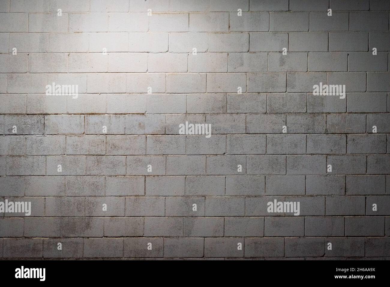Parete bianca a blocchi invecchiata dall'umidità e illuminata con luce a soffitto. Sfondo. Foto Stock