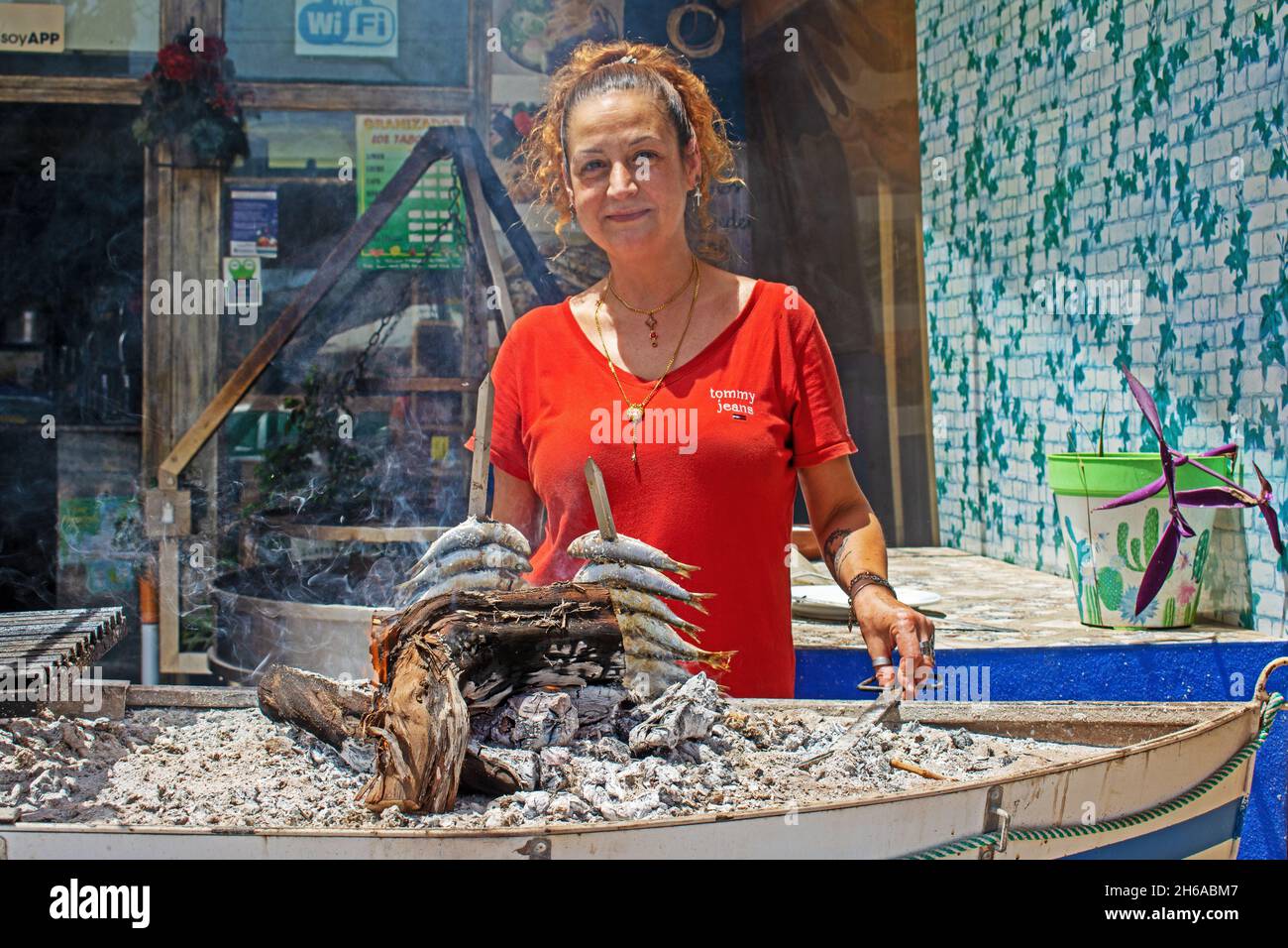 Signora spagnola grigliare sardine sul fuoco di legno nel Mediterraneo bar / ristorante costiero, Puerto de Mazarrón, Murcia, Spagna. Foto Stock