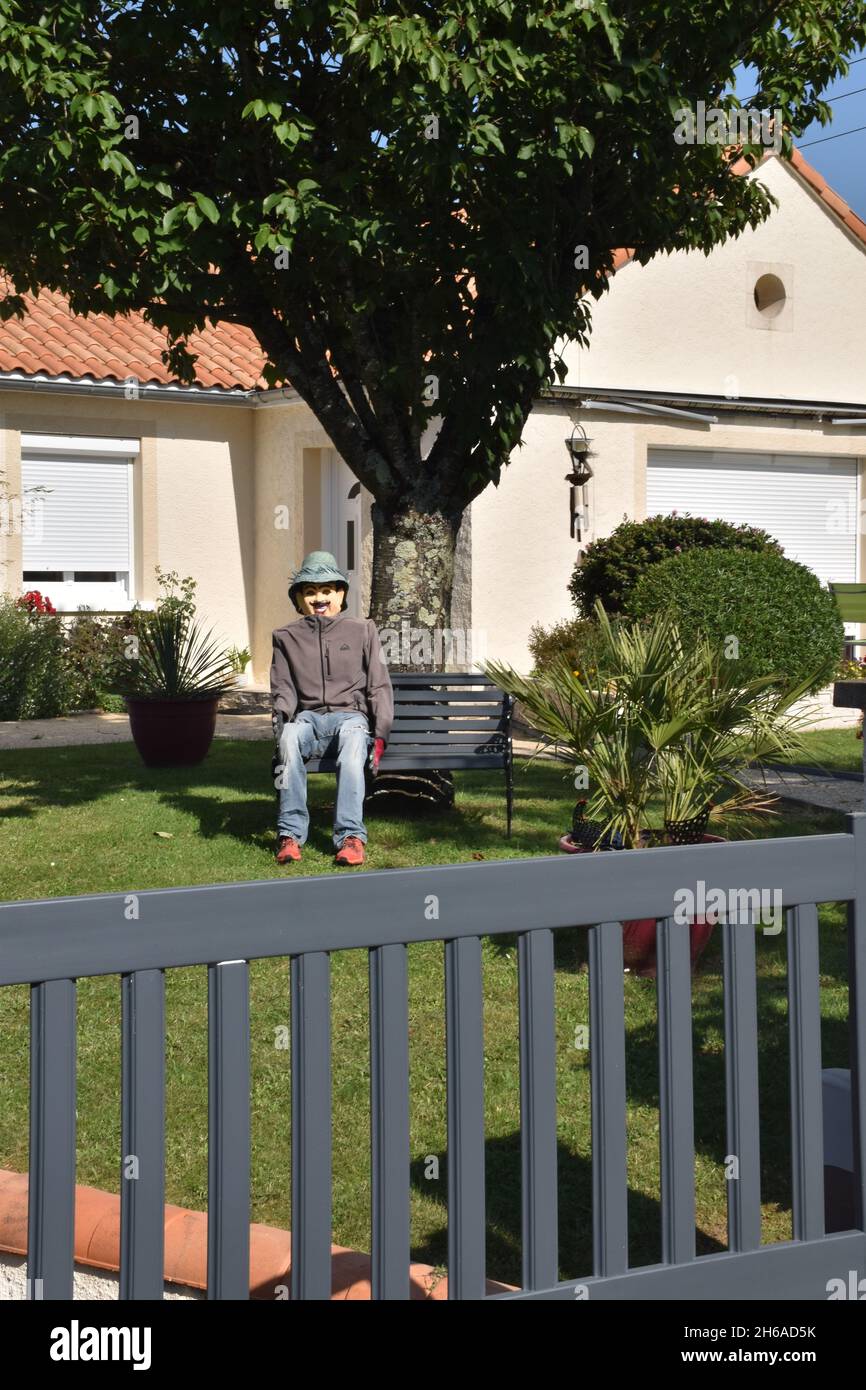 Un uomo di paglia, una figura umanoide piuttosto cremosa, piena di dimensioni, che si rilassa su una panca, in un giardino suburbano al limitare della città Foto Stock