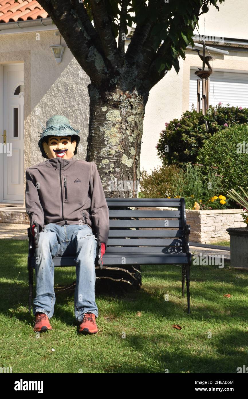 Un uomo di paglia, una figura umanoide piuttosto cremosa, piena di dimensioni, che si rilassa su una panca, in un giardino suburbano al limitare della città Foto Stock