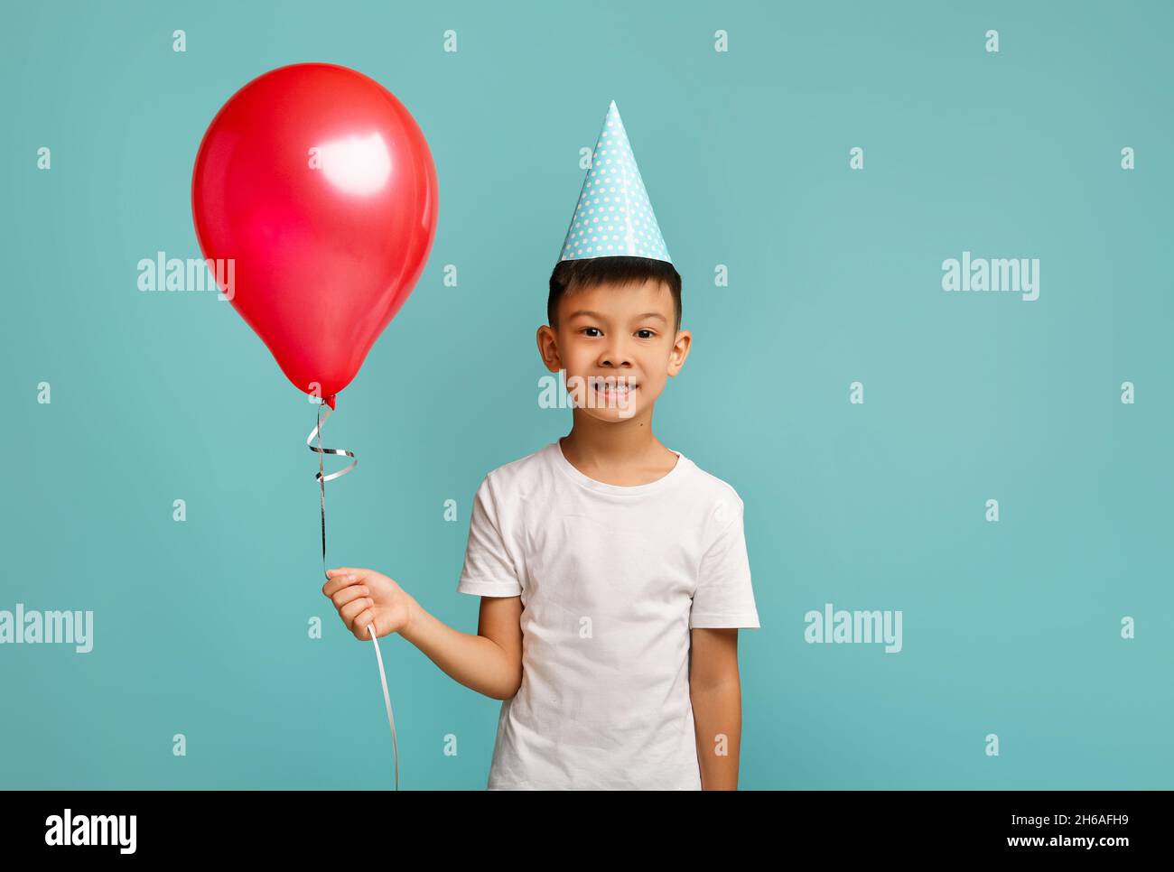 Festa del B-Day. Ritratto di eccitato felice ragazzo asiatico poco che tiene Red Baloon, cheerful coreano maschio Kid indossare cappello partito festeggiamento compleanno, pos Foto Stock