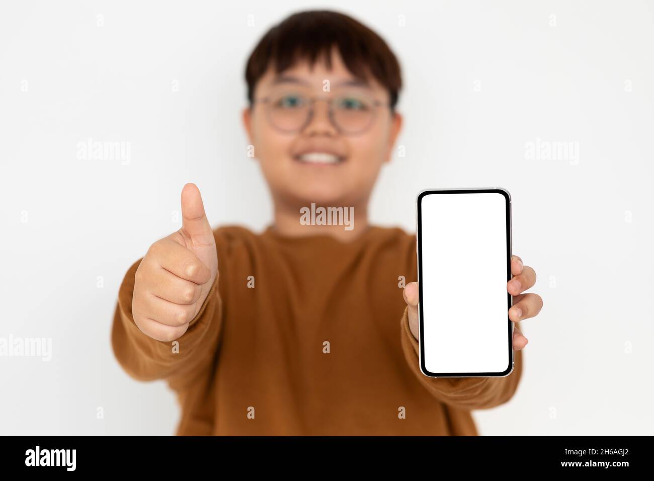 Allegro ragazzo asiatico ragazzo chubby adolescente indossare occhiali mostrando moderno smartphone con schermo vuoto e pollice su, raccomandare più recente divertente mobile a Foto Stock
